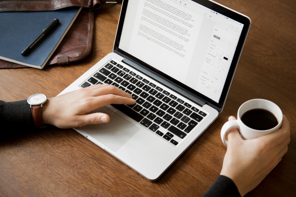 man-sitting-at-a-wooden-desk-working-at-home-office-or-cafe-on-a-laptop-computer-with-notebook-pen_t20_1boaAY